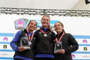 Claire Buhrfeind standing center podium after placing first in junior bouldering finals, along side Maya Madere (left), second place, and Johanna Holfeld (right), third place. Photo: Eddie Fowke.